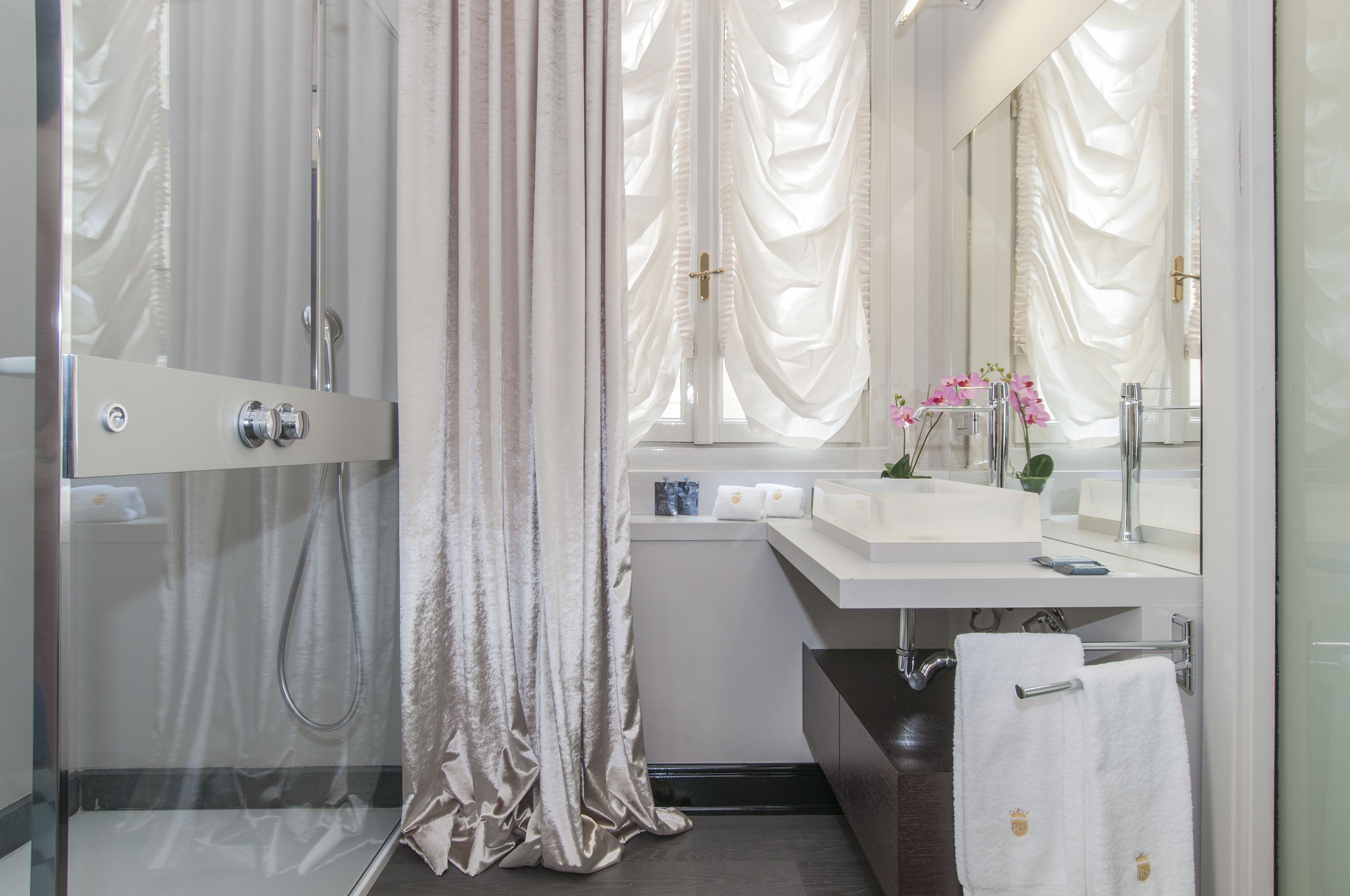 Un bagno moderno con cabina doccia in vetro, un mobile lavabo bianco con specchio e un porta asciugamani.