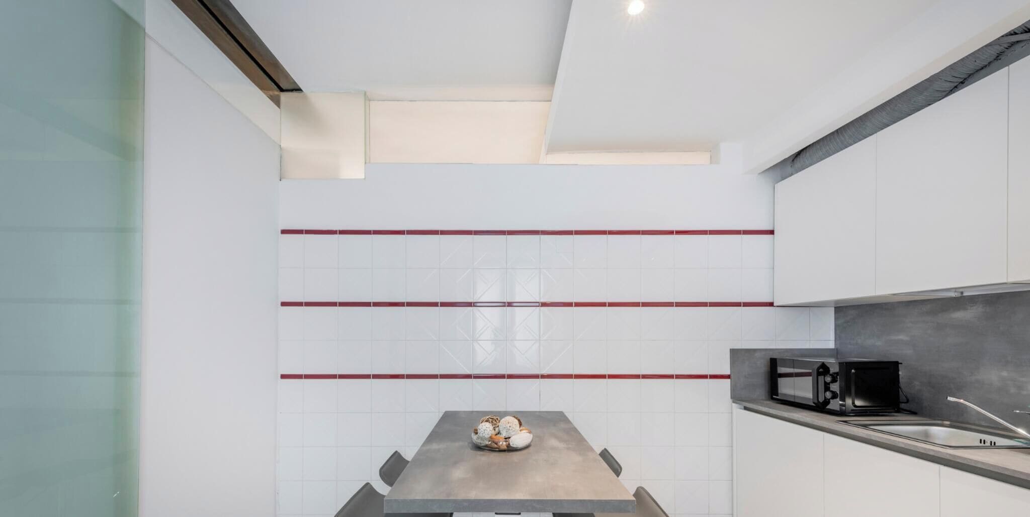 A modern kitchen with white cabinets, a stainless steel countertop, and a microwave.