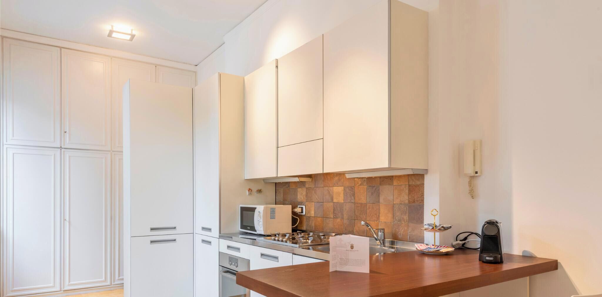 A modern kitchen with white cabinetry, a wooden countertop, a microwave, and a stove.