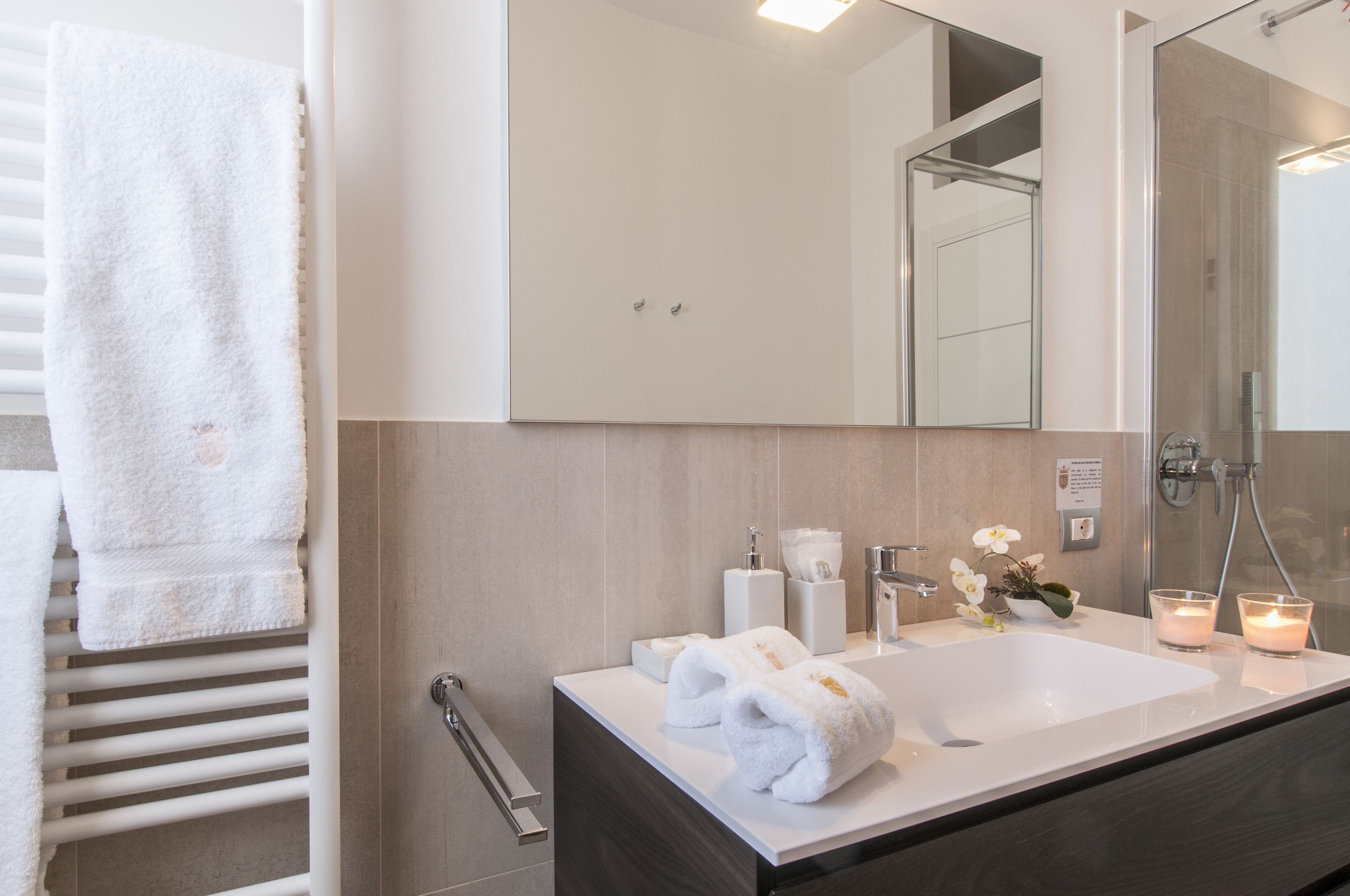 A modern bathroom with a large mirror, white sink, and two candles.