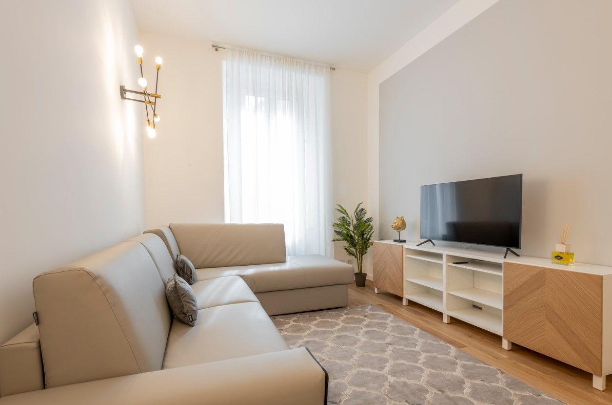 A modern living room with a beige sofa, a flat-screen TV on a wooden stand, and a potted plant.