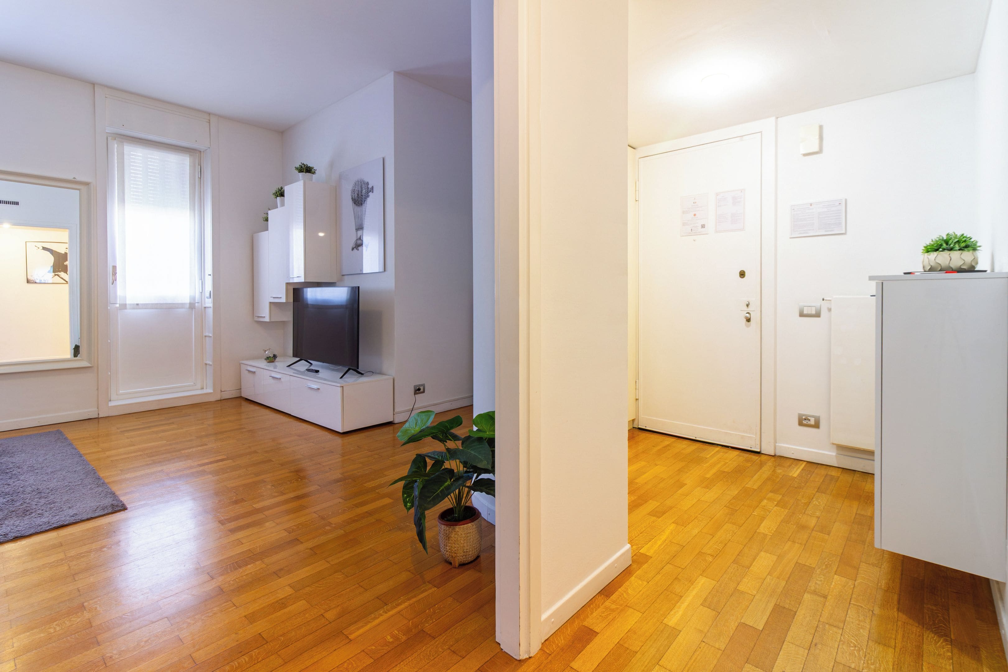 A modern living room with a flat-screen TV, white cabinets, and a wooden floor.