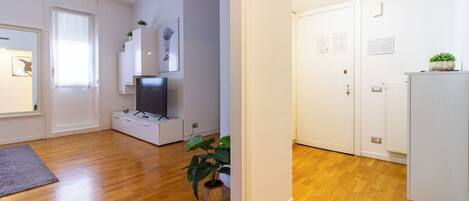 A modern living room with a flat-screen TV, white cabinets, and a wooden floor.