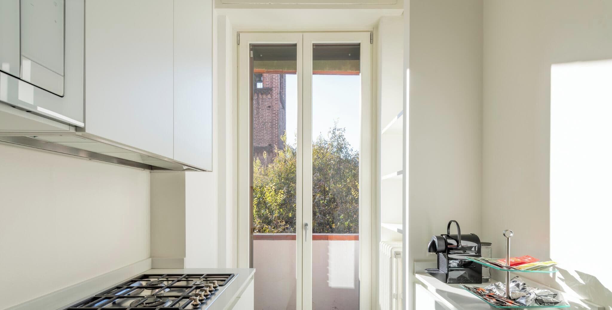 A kitchen with a gas stove, a coffee machine, and a glass table with items on it.