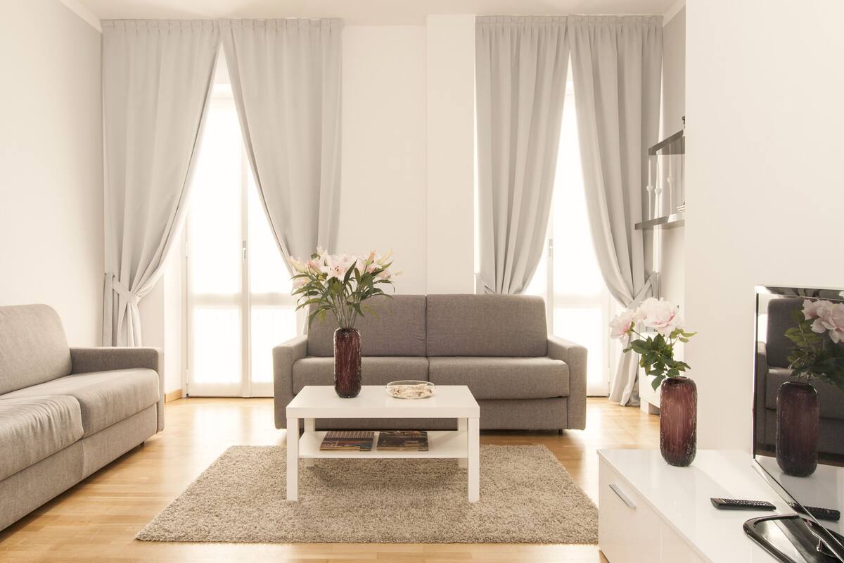 A modern living room with a grey sofa, a white coffee table, and a TV on a stand.
