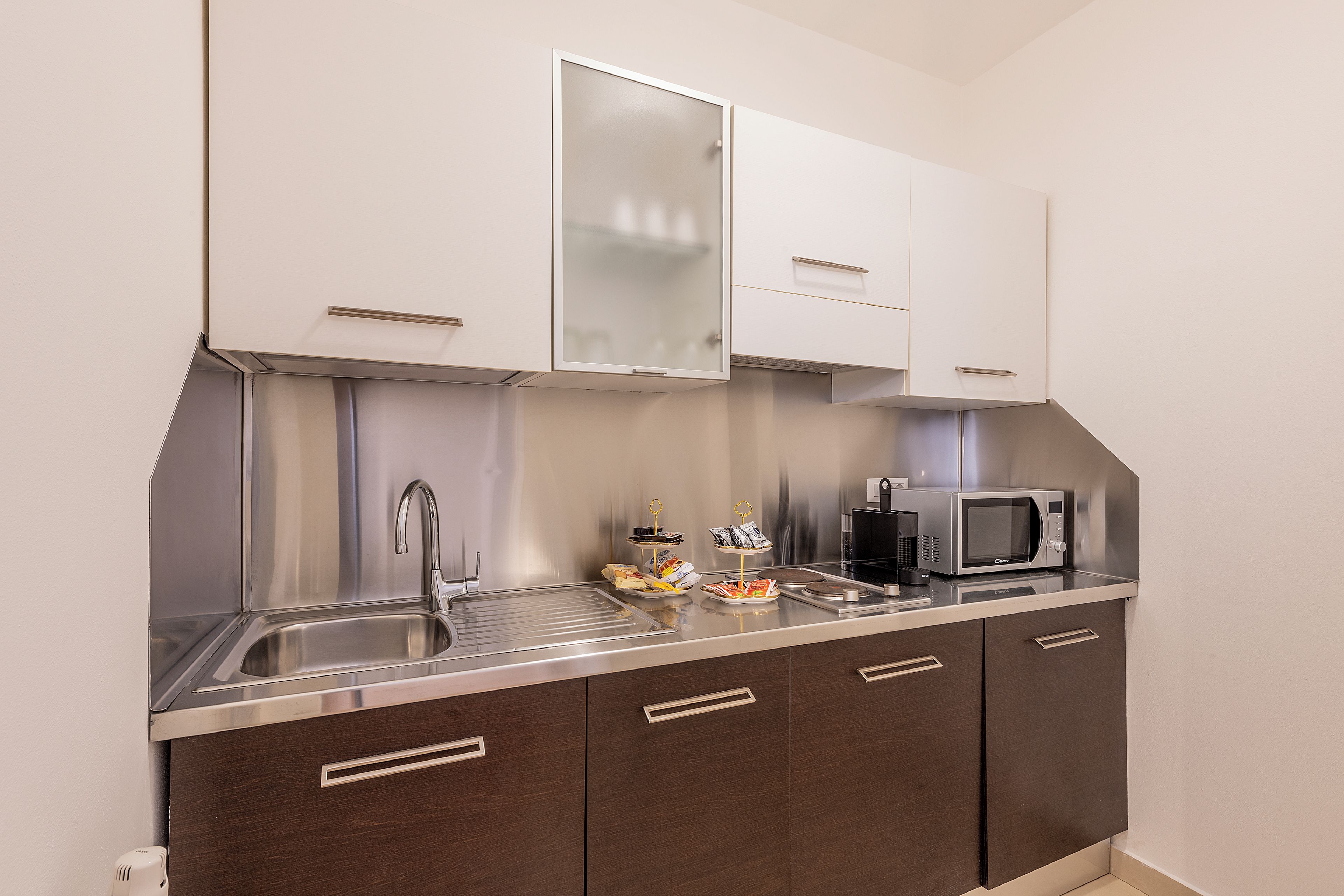 A compact kitchenette with a stainless steel sink, a microwave, and a small countertop with snacks.