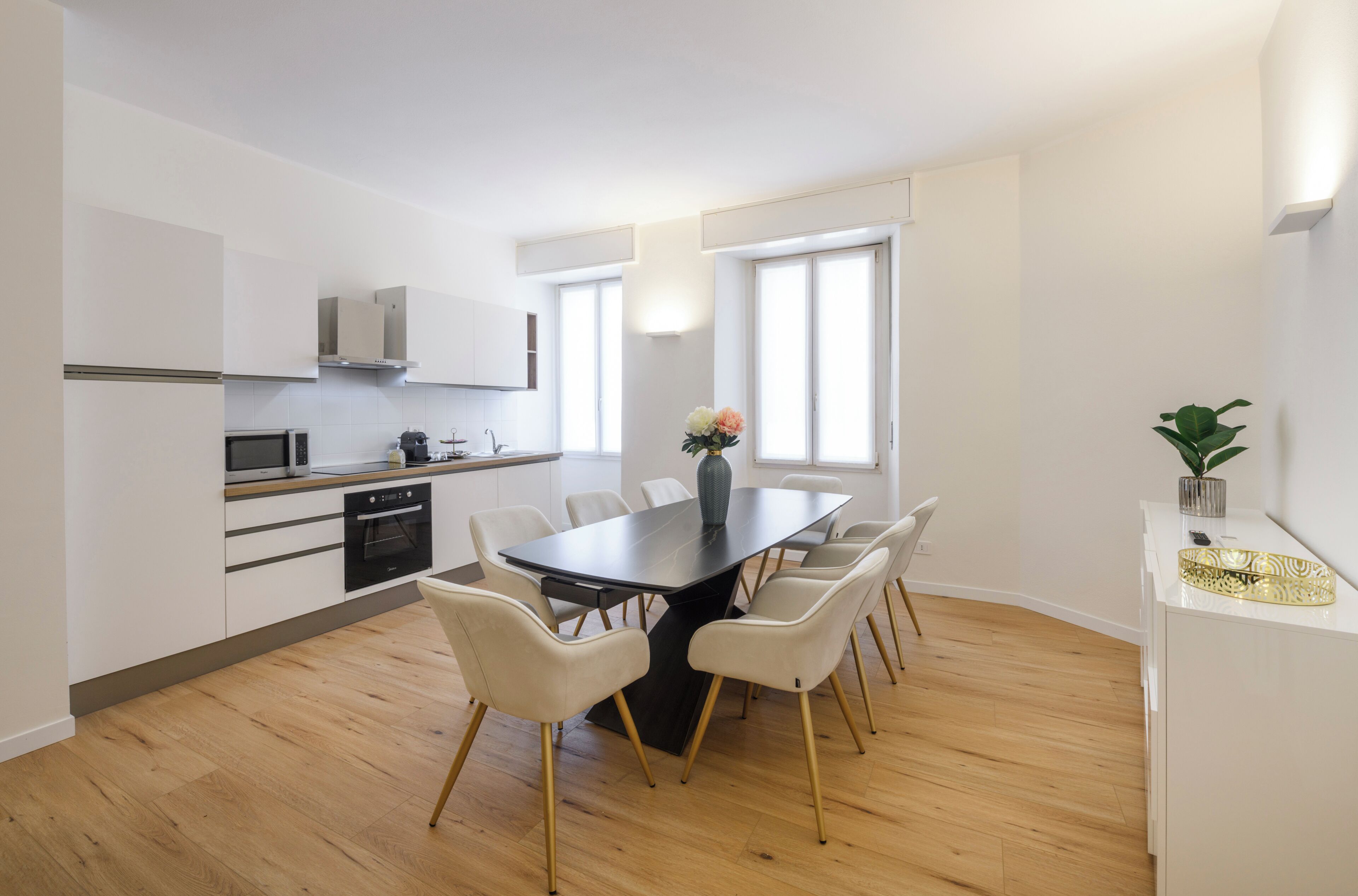 A modern kitchen with white cabinets, a microwave, and a stove. There is a dining table with chairs and a vase with flowers.