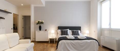 A modern bedroom with a bed, bedside tables, a white sofa, and a large window.