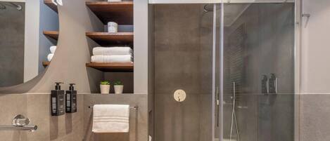 A modern bathroom with a glass-enclosed shower, wooden shelves with towels, and toiletries.
