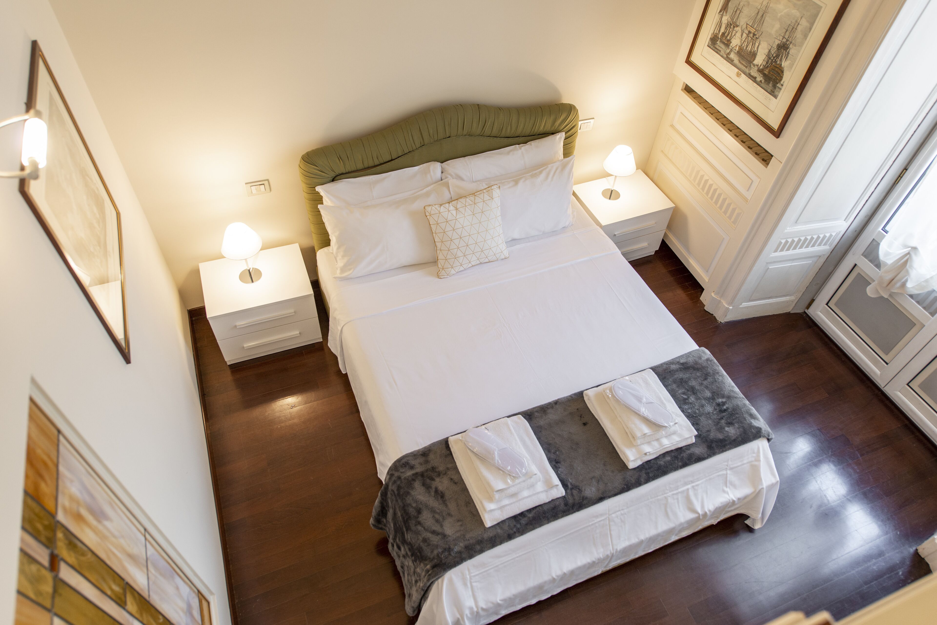 A neatly made bed with white linens, a green headboard, and two bedside lamps.