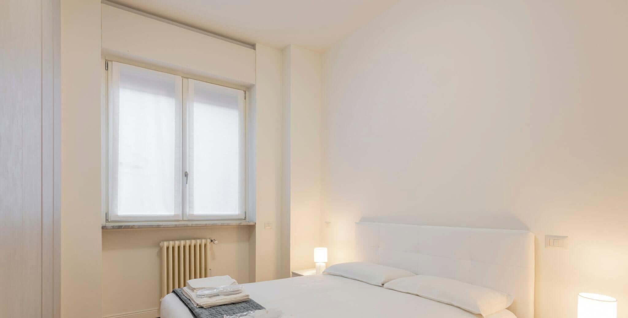 Une chambre à coucher avec un lit, des lampes de chevet, un radiateur et une fenêtre.