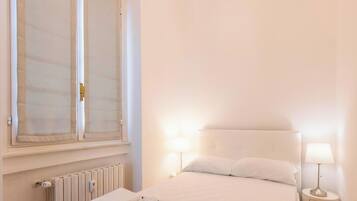 Una camera da letto con un letto, due lampade da comodino, una finestra con tende e un termosifone.