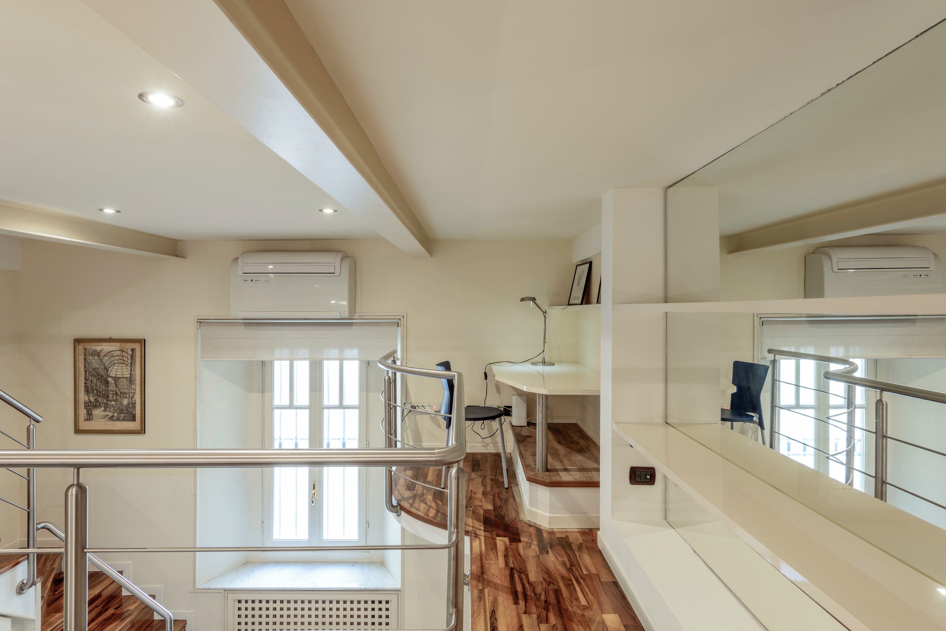 A modern hotel room with a wooden floor, a balcony with a metal railing, a large mirror, and an air conditioning unit.