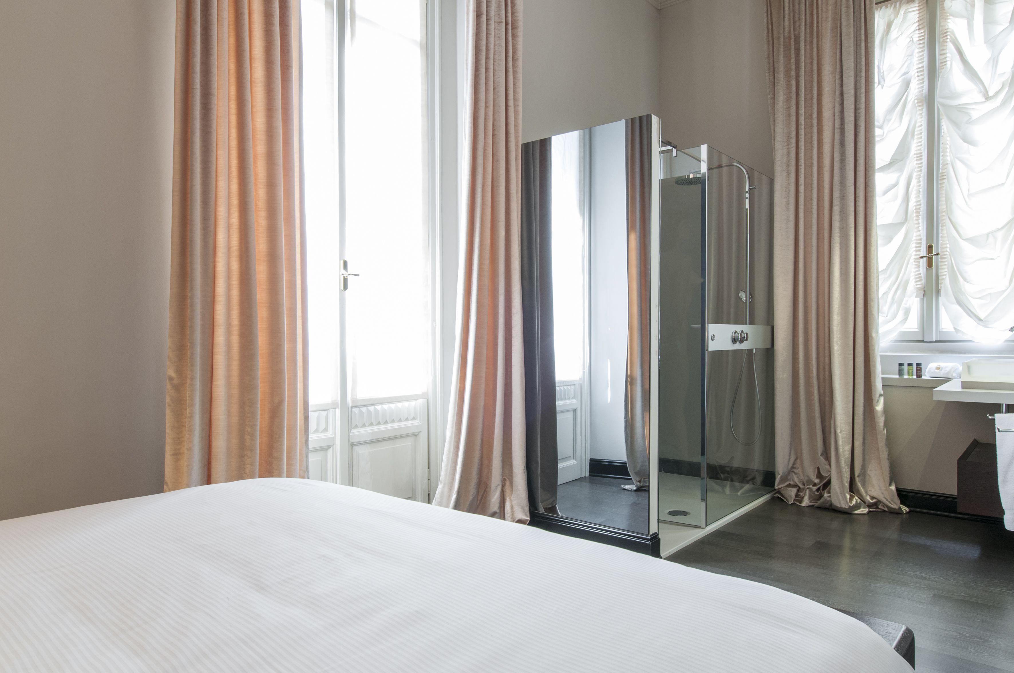 A hotel room with a bed, a glass-enclosed shower, and a bathroom with a sink and mirror.