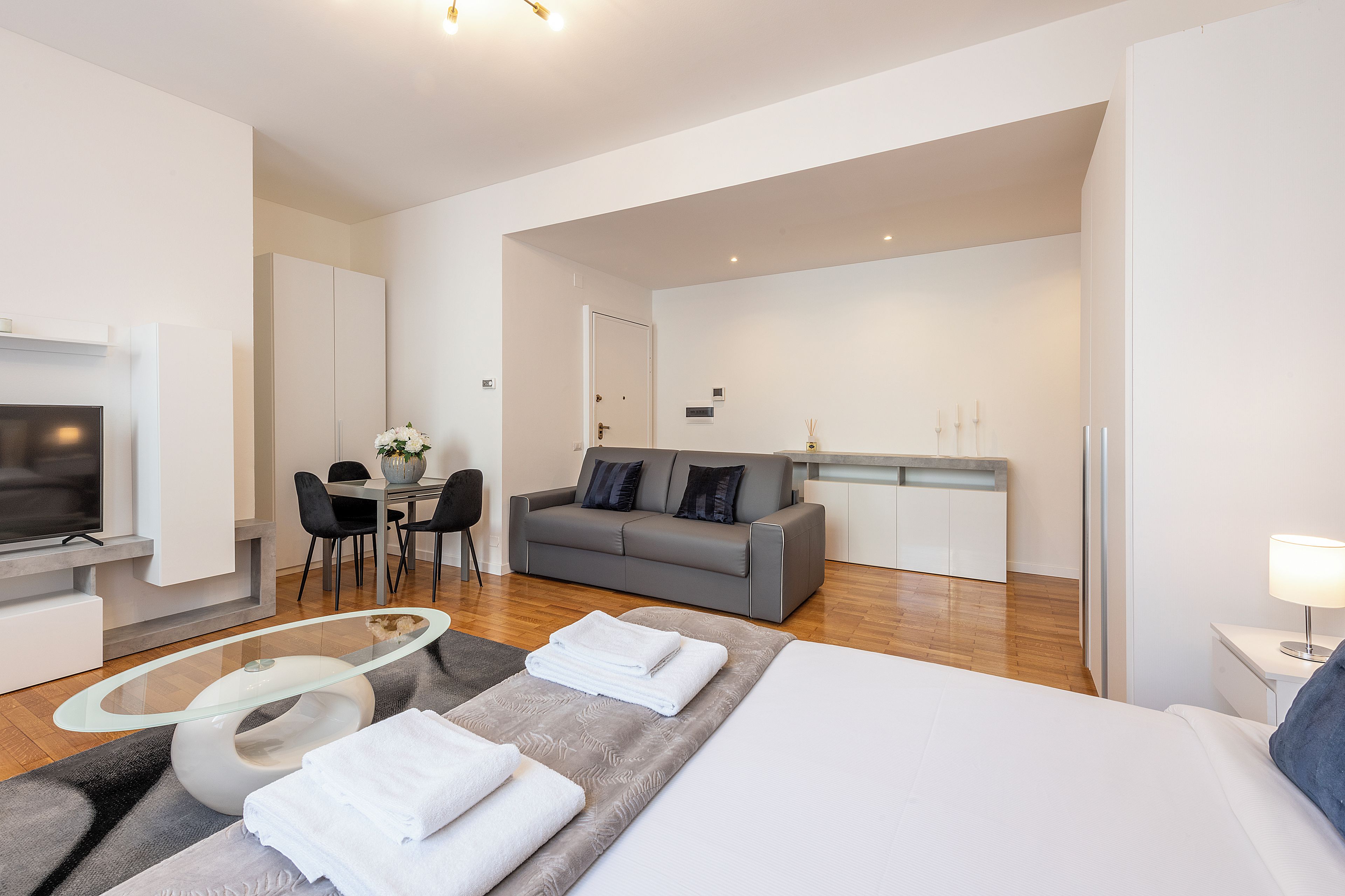 A modern hotel room with a bed, a sofa, a dining area, and a TV.