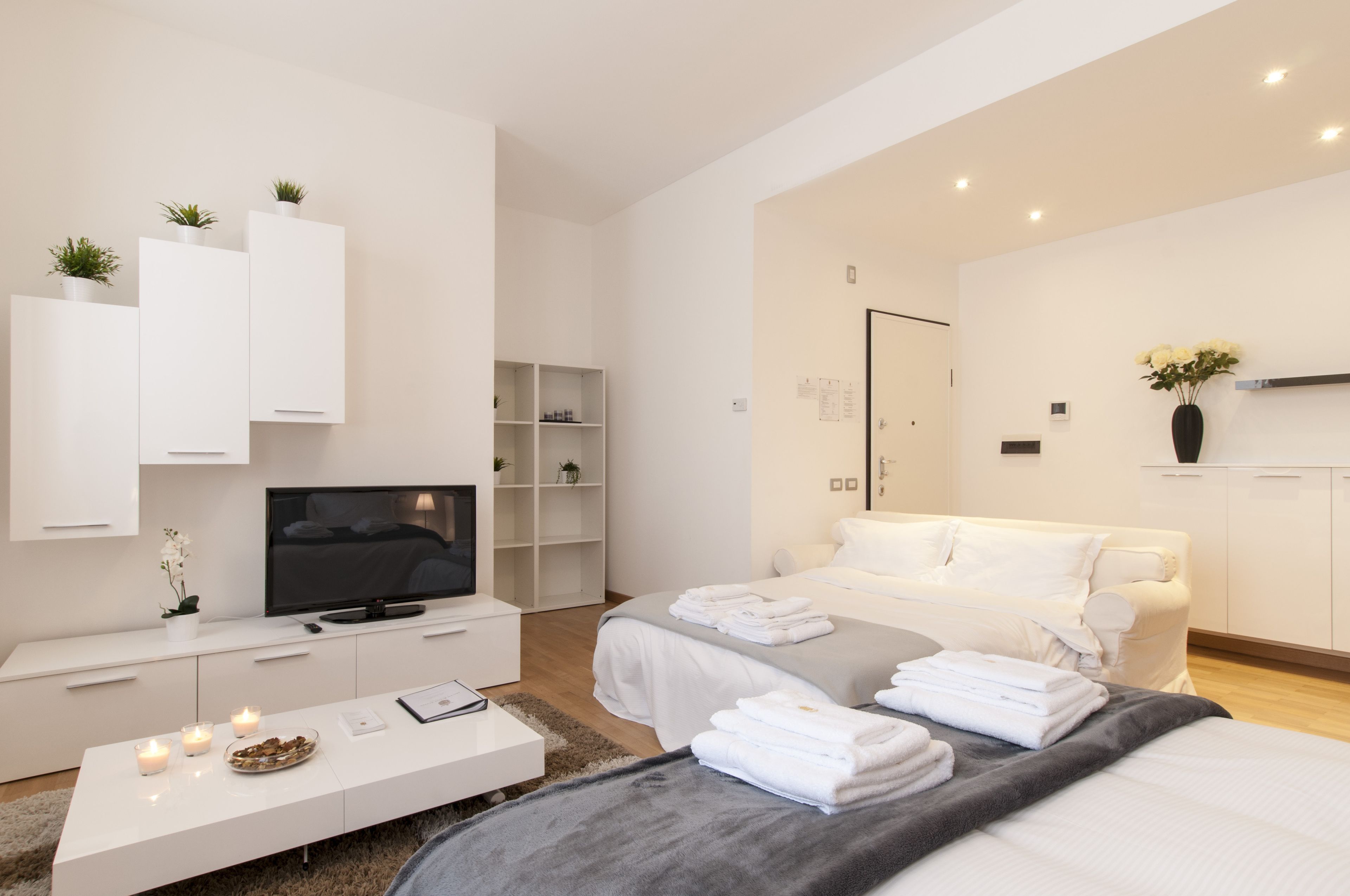 A modern hotel room with a bed, a TV, a white console, and a small seating area with a table and candles.