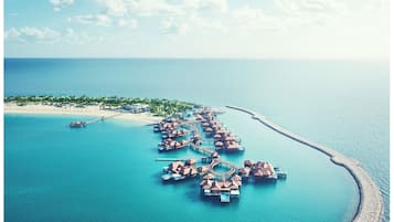 Overwater bungalows connected by walkways, situated on a sandy beach amidst lush greenery.