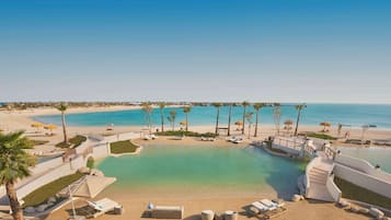 Um resort com uma piscina grande, área de praia e palmeiras.