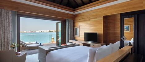 A hotel room with a large bed, a TV, a desk, and a view of the sea.