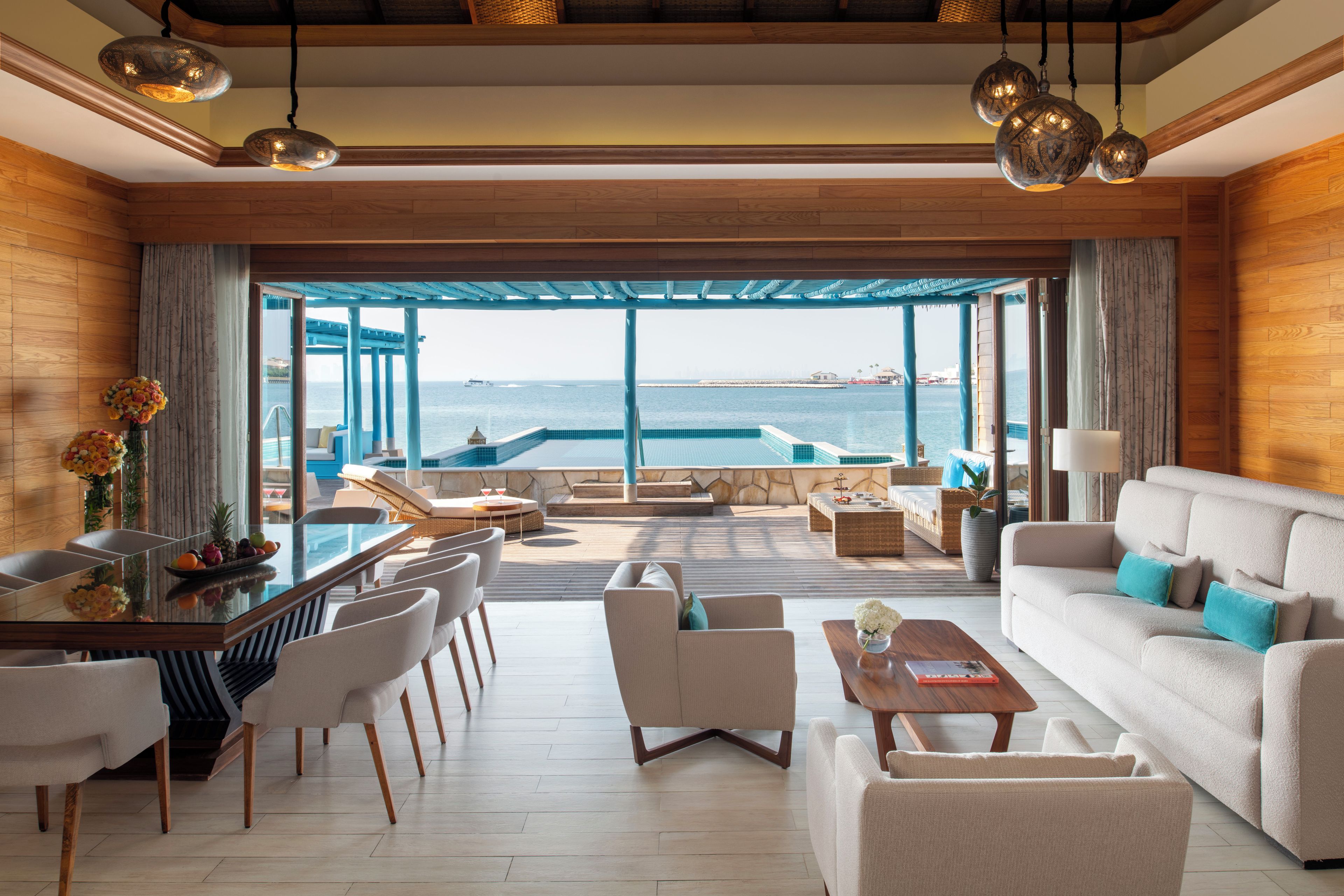 Ein modernes Wohnzimmer mit Blick auf das Meer, einem Pool und einem Essbereich mit Bar.