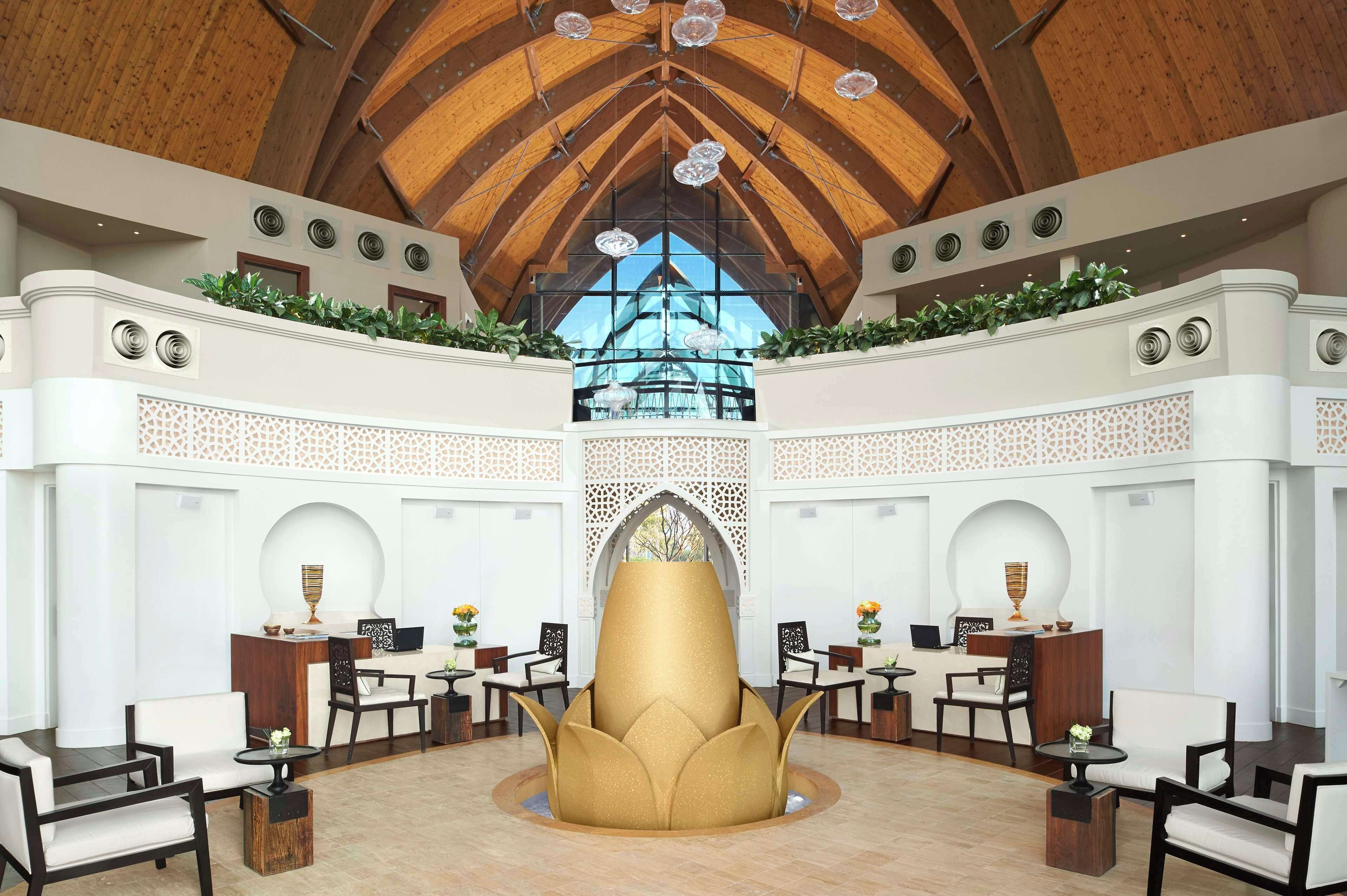 A spacious lobby with a high wooden ceiling, a central decorative fountain, and a view through a large window.