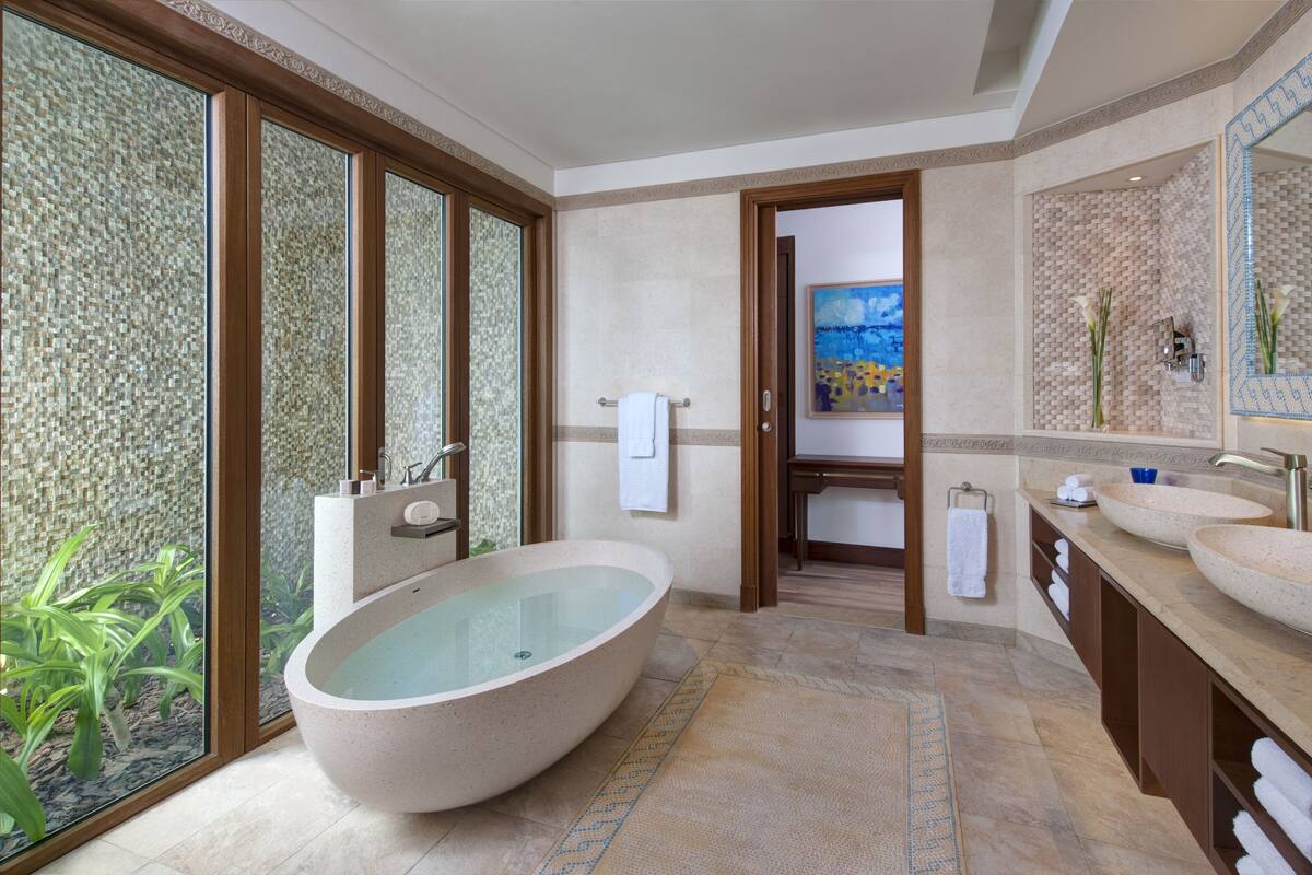 Een ruime badkamer met een vrijstaand ligbad, een wastafel met twee kommen en een grote spiegel.