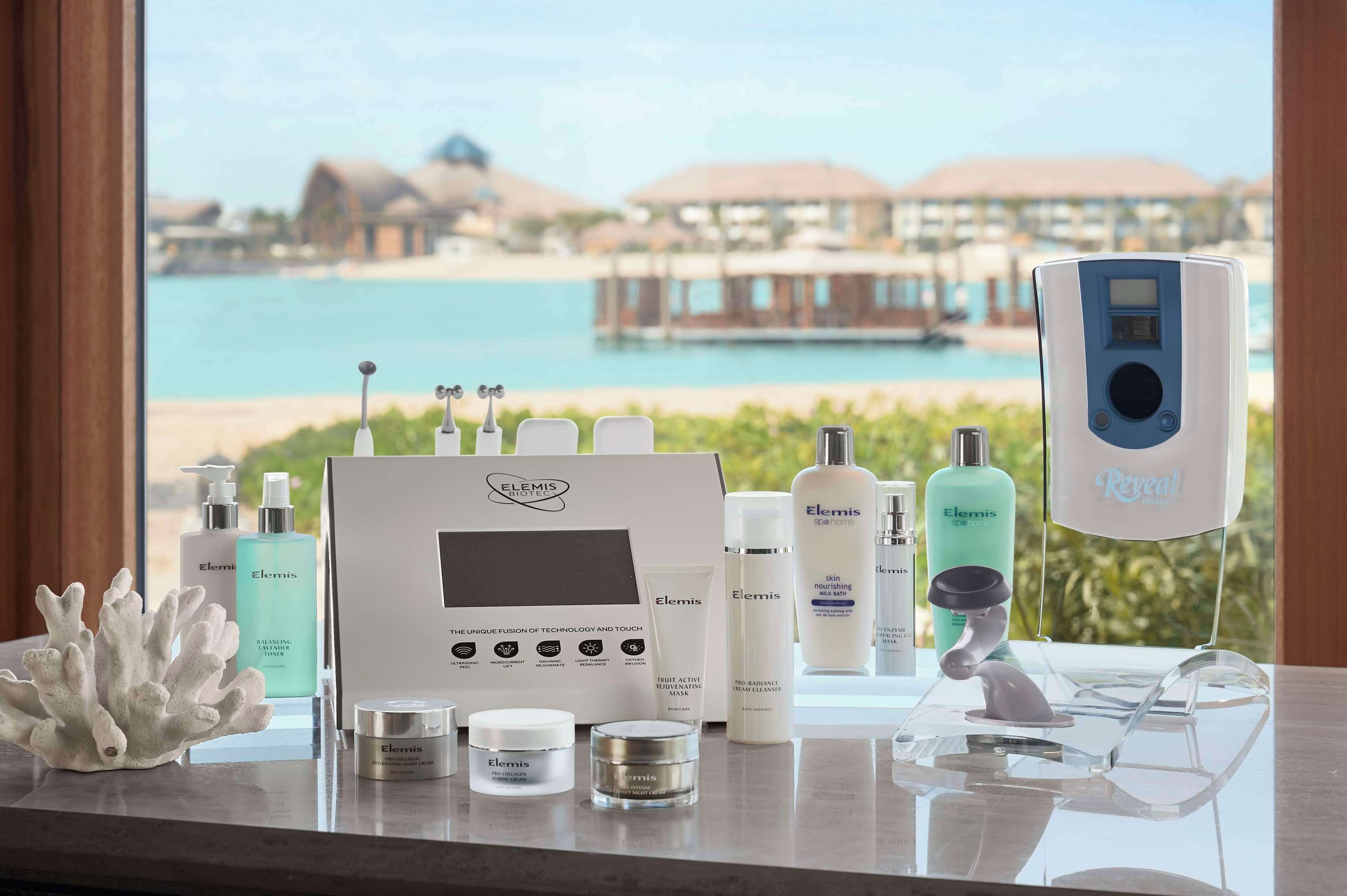A skincare display with Elemis products, a facial cleansing device, and a view of a beach resort.