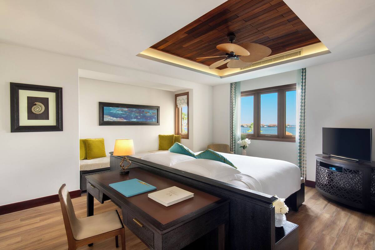 Een hotelkamer met een bed, bureau, stoel, televisie en uitzicht op zee.