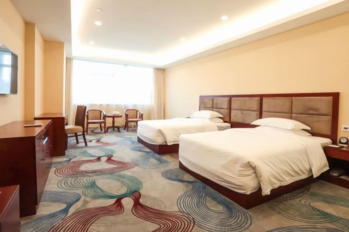 A hotel room with two beds, a desk, and a chair.