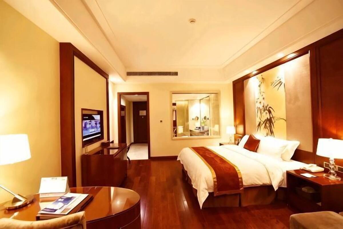 A hotel room with a bed, a desk, a TV, and a mirror.