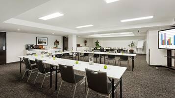 Un salón de conferencias con mesas blancas, sillas negras y una pantalla proyectando un gráfico de barras.