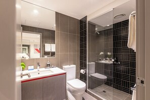 A modern bathroom with a glass-enclosed shower, a white toilet, and a vanity with a mirror.