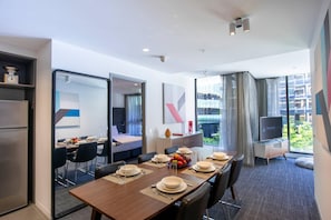 Moderni hotellihuone, jossa on ruokailutila, sänky, televisio ja parveke, jolta on näkymä kaupunkiin.