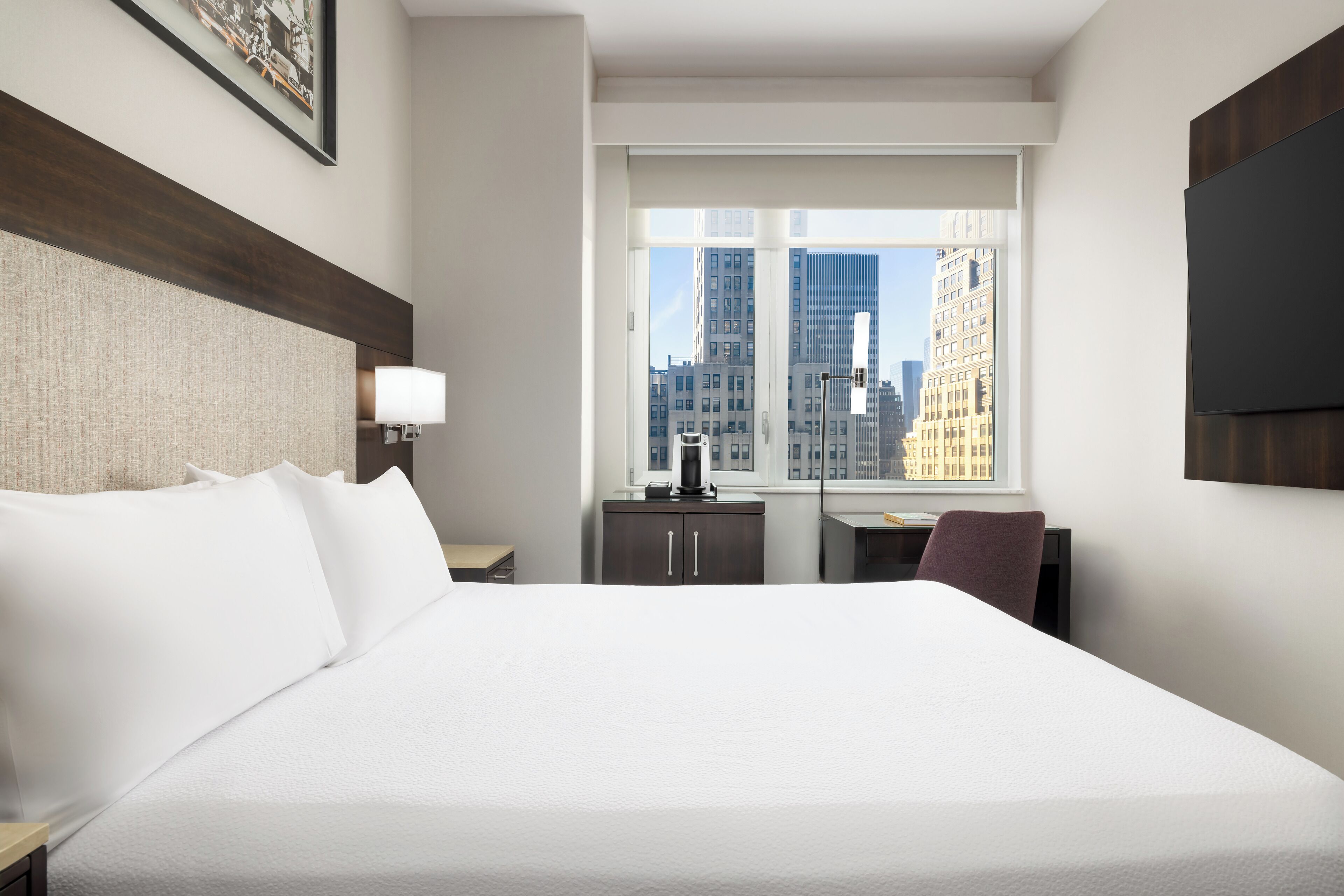 Ein Hotelzimmer mit einem großen Bett, einem Schreibtisch, einem Stuhl und einem Fenster mit Blick auf die Stadt.