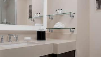 A modern bathroom with a large mirror, two sinks, and glass shelves holding toiletries and towels.