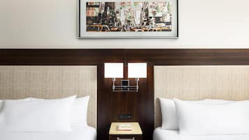 A hotel room with two beds, a framed cityscape picture, a nightstand with a book, and a control panel.
