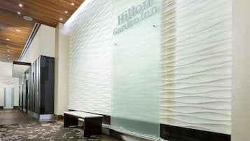 Welcome to the Hilton Garden Inn, featuring a modern reception area with a glass partition, wooden ceiling, and unique wall designs.