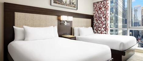 A hotel room with two beds, a large window with a city view, a framed picture on the wall, and a patterned curtain.