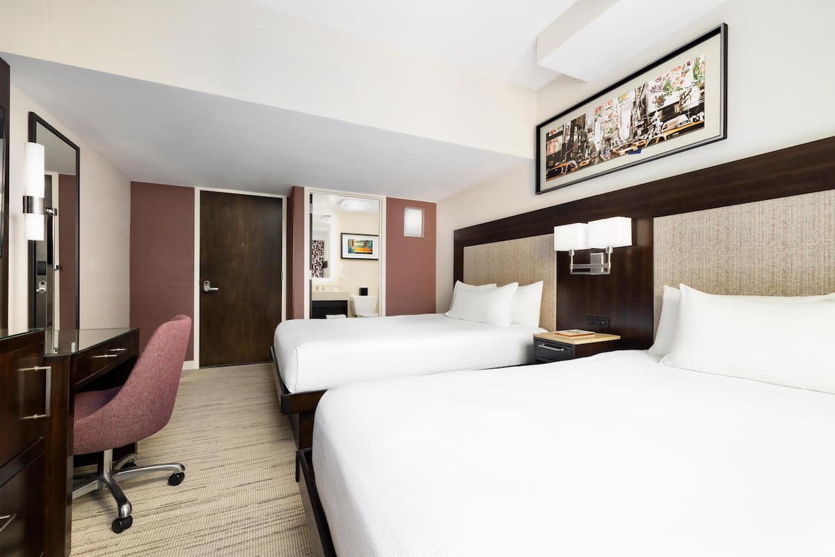 Habitación de hotel con dos camas, un escritorio, una silla y un cuadro grande en la pared.