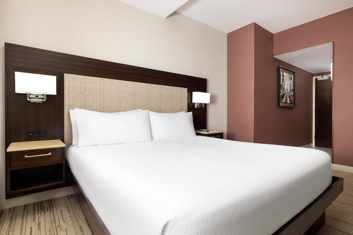 Una habitación de hotel con una cama grande, mesitas de noche y una lámpara de pared.