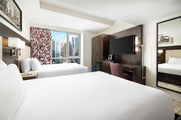 A hotel room with a large bed, a desk with a chair, a flat-screen TV, and a large window with a city view.