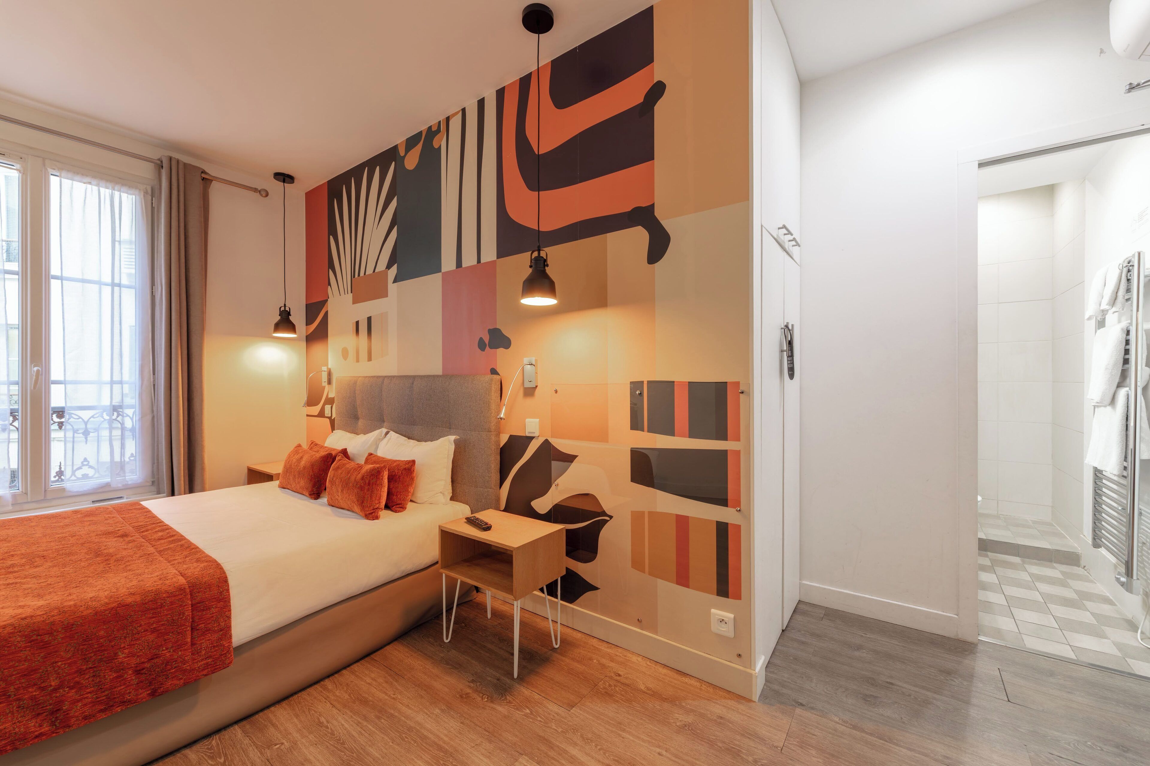 A modern hotel room with a large bed, a bedside table, a nightstand, and a wall with abstract art.