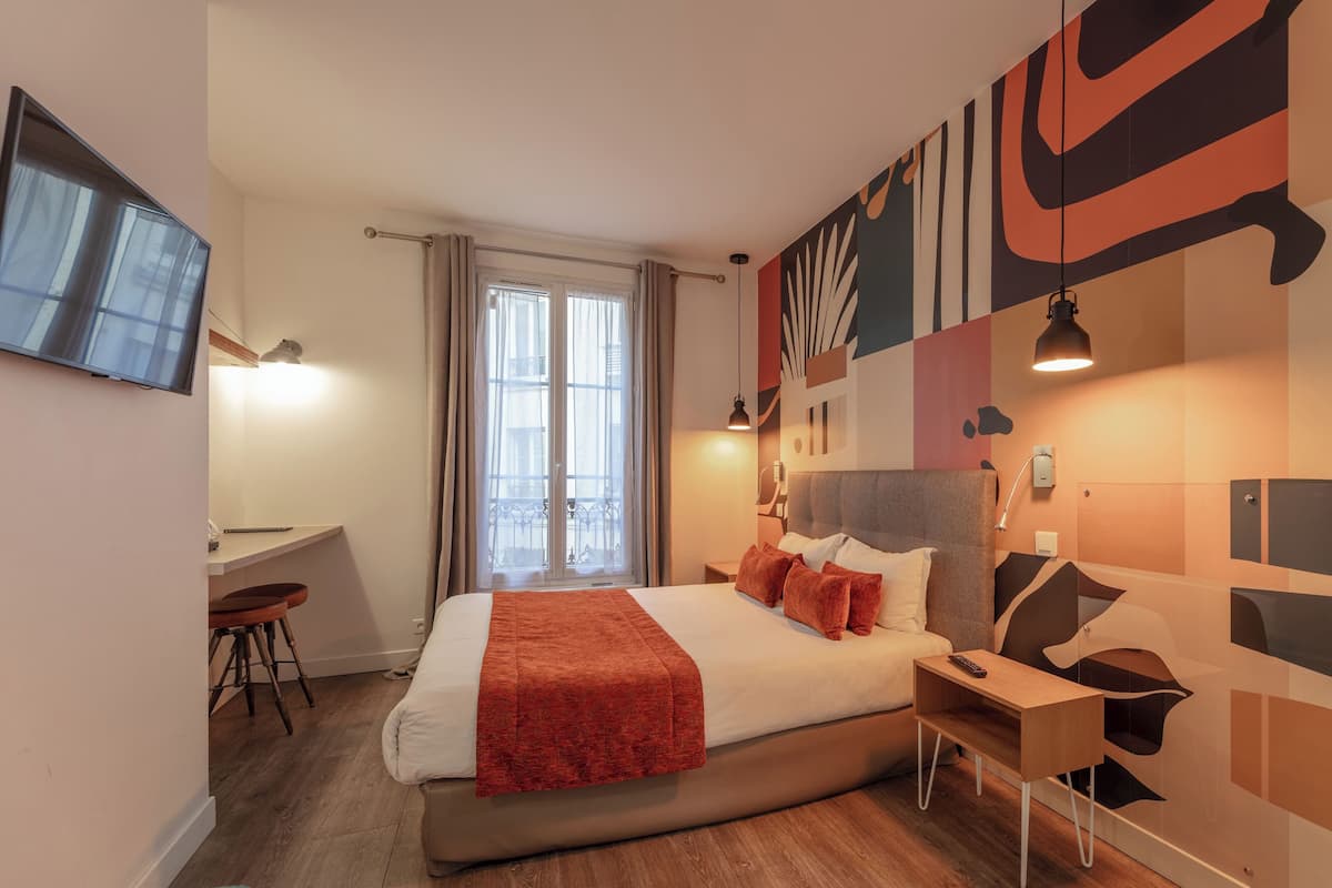 A modern hotel room with a bed, desk, and chair, a TV mounted on the wall, and a large window with curtains.