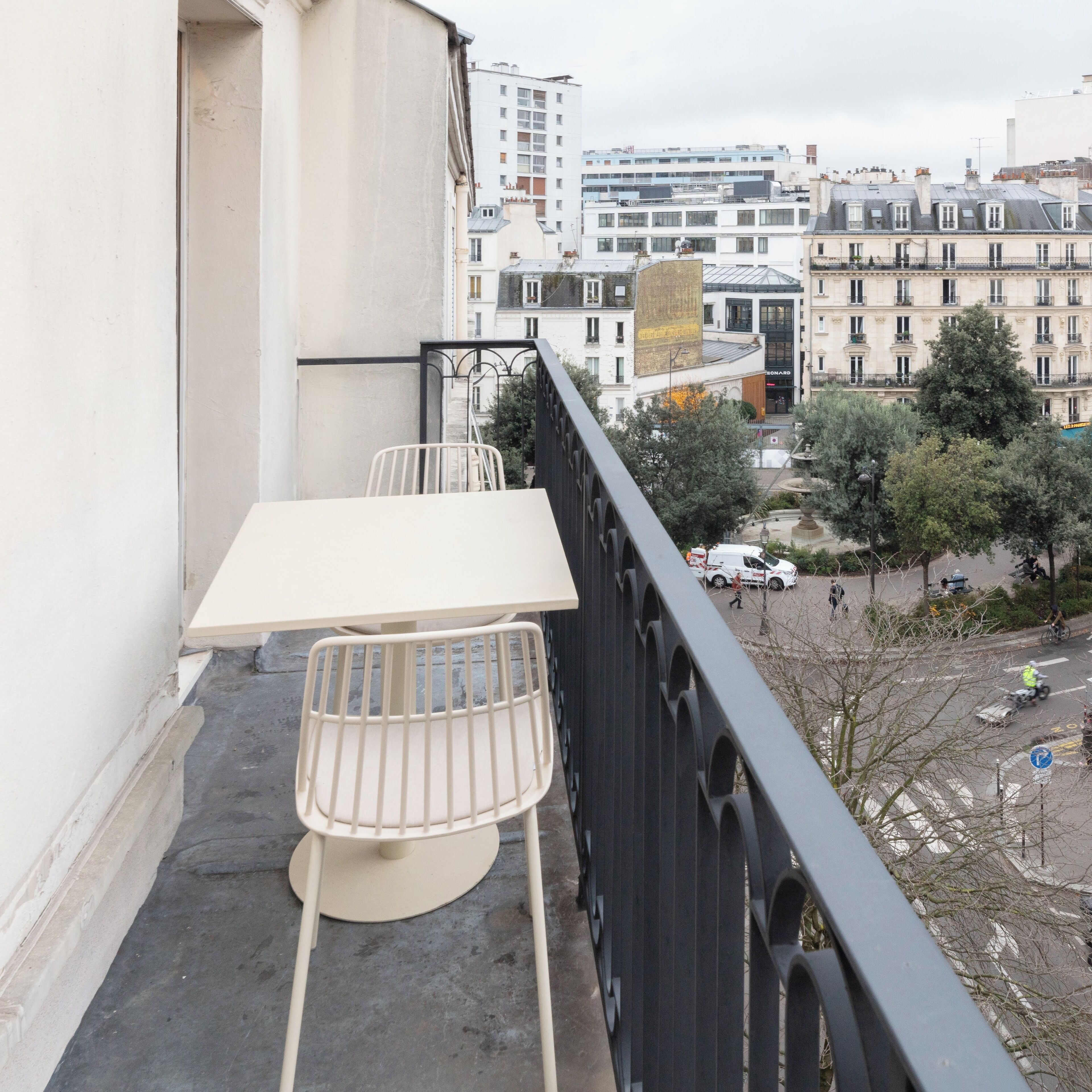 A balcony with a table and chairs, overlooking a cityscape with buildings and trees.