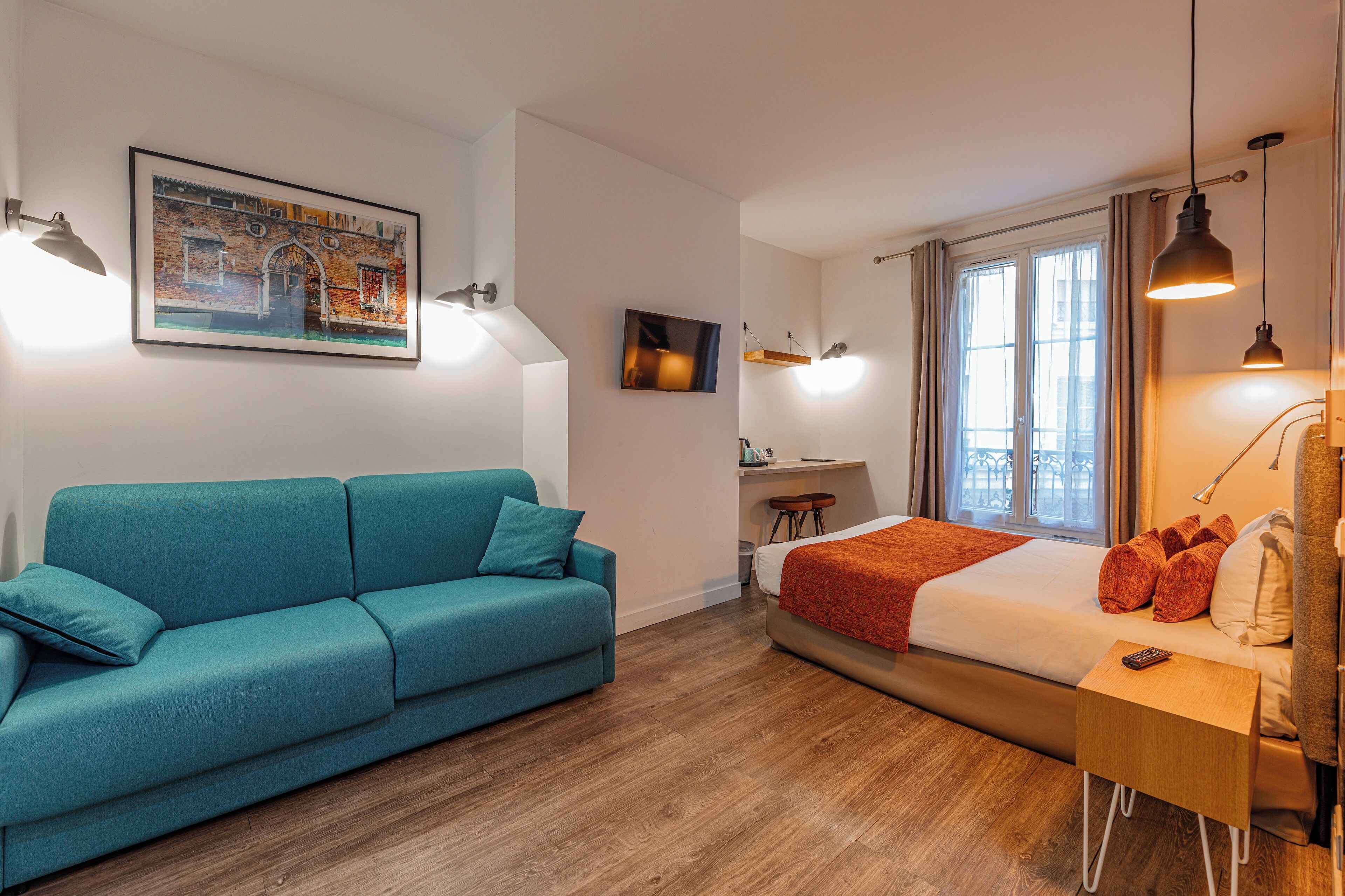 Una habitación moderna con un sofá color turquesa, una cama con una colcha roja, un escritorio y una ventana con cortinas.