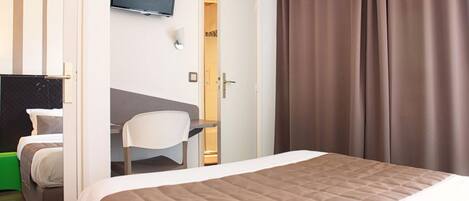 A hotel room with a bed, a desk, a chair, a TV, and a wardrobe.
