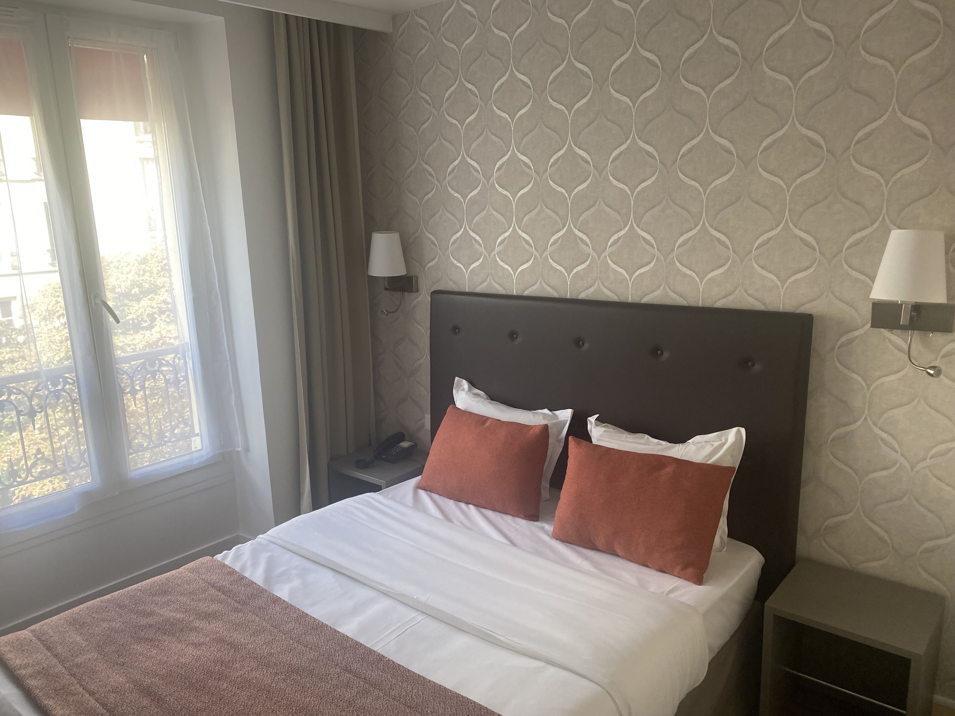 A hotel room with a bed, a nightstand, a lamp, and a window with curtains.
