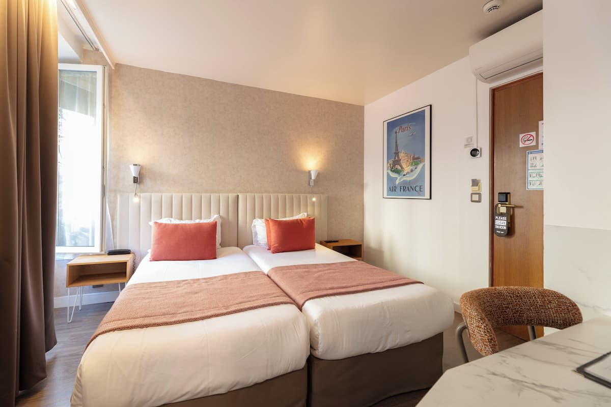 A hotel room with two beds, a desk, a chair, and a view of the Eiffel Tower.