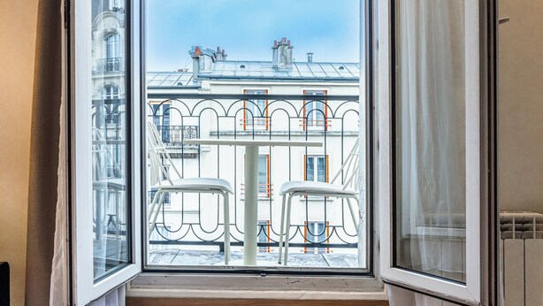 A hotel room with a large sliding glass door leading to a balcony with a view of the cityscape. - Hotel De Venise (Paris)