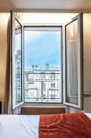 A hotel room with a large sliding glass door leading to a balcony with a view of the cityscape. - Hotel De Venise (Paris)